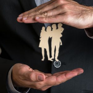 Insurance agent making protecting gesture around a paper cut silhouette of a family